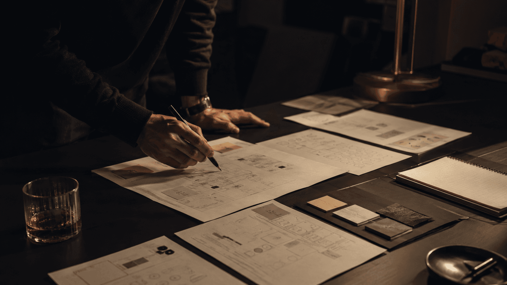 Hands drafting product layouts across a dark studio desk