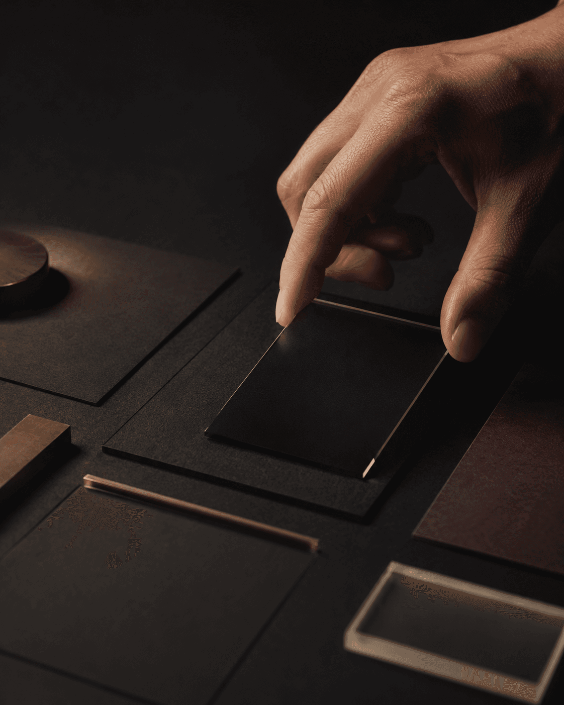 A hand placing a dark material sample among precise studio objects